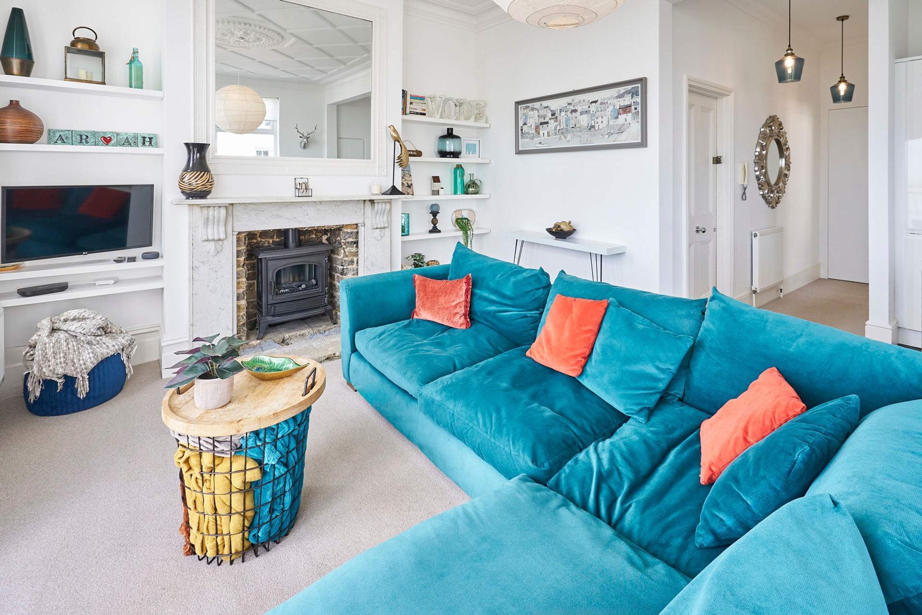 A living room with a teal sofa, a fireplace, a television, and various decorative items on shelves.