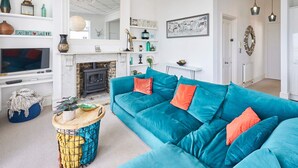 Un salon avec un canapé de couleur turquoise, une cheminée, un téléviseur et divers objets décoratifs disposés sur des étagères.