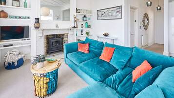 A living room with a teal sofa, a fireplace, a television, and various decorative items on shelves.