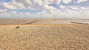 Une plage de galets avec une jetée en bois qui s’avance dans l’eau.