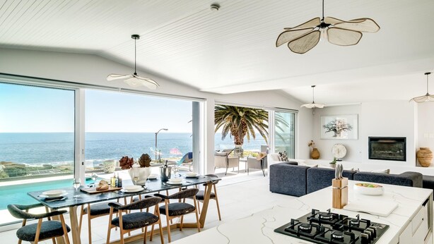 Eine moderne Küche mit einer großen Kochinsel, einem Essbereich mit Meerblick und einem Wohnbereich mit Sofa und Fernseher.