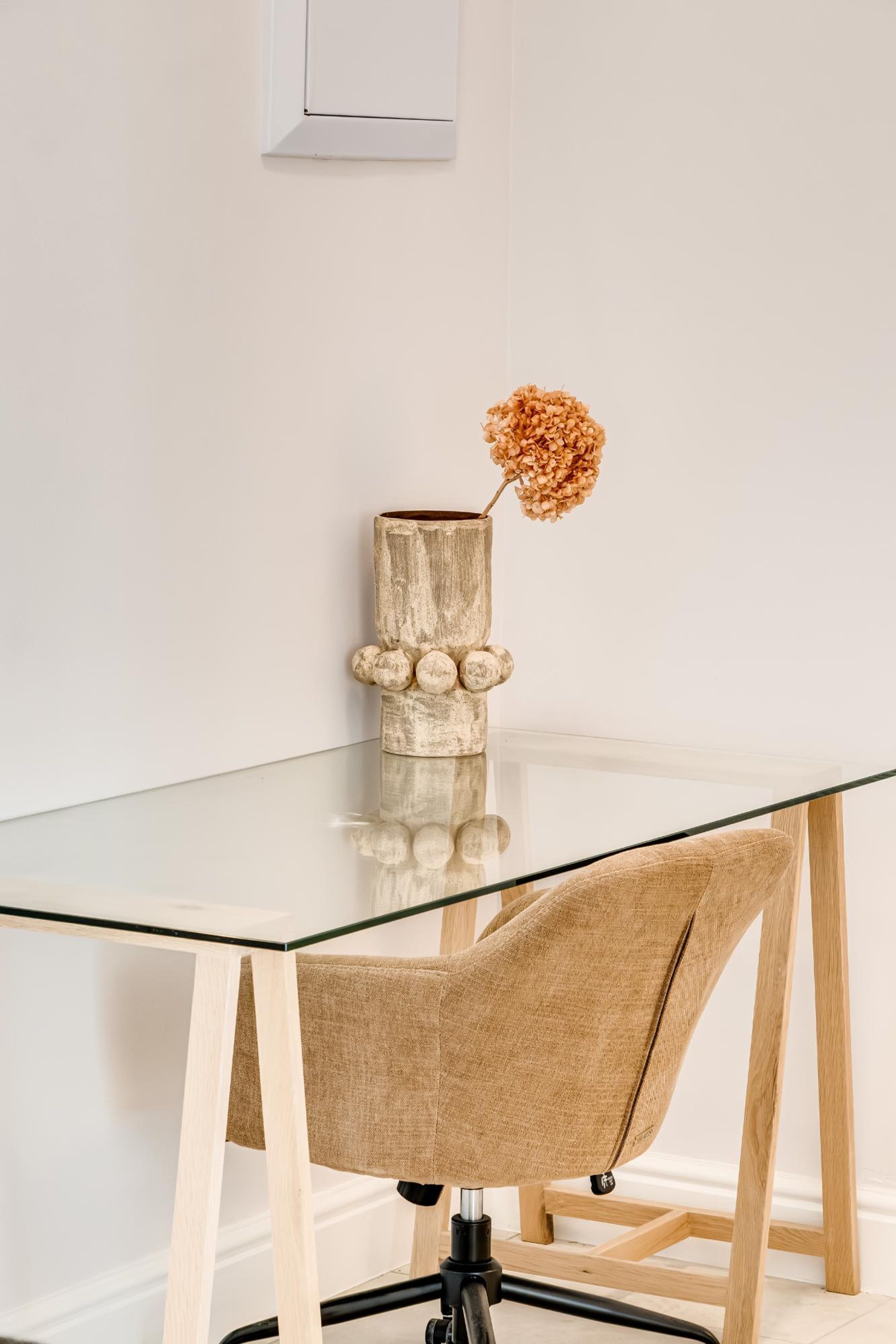 A modern dining area with a glass table, wooden chairs, and a decorative vase with dried flowers.