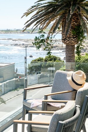 A balcony with a view of the ocean, a palm tree, and a chair with a hat.