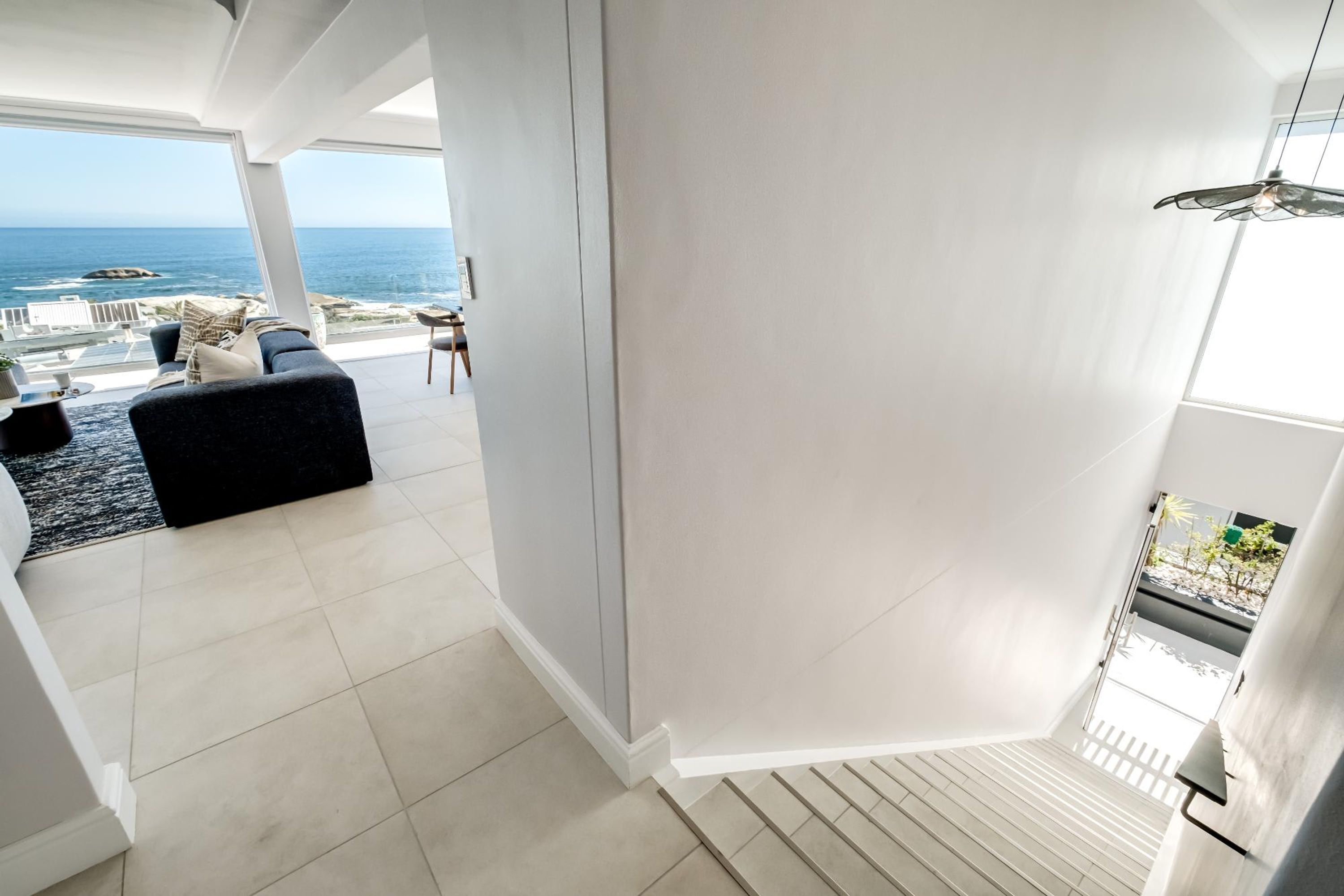 A modern interior with a view of the ocean, a staircase, and a seating area with a black sofa.
