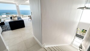 Un intérieur moderne avec vue sur l’océan, un escalier et un coin salon agrémenté d’un canapé noir.