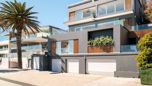 Un immeuble résidentiel moderne à plusieurs étages, doté d’un balcon, de portes de garage et d’un palmier.