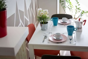 Et spisebord dækket med tallerkener, kopper og en kaffekande, omgivet af stole.