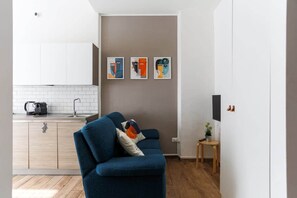 En moderne stue med en blå sofa, et lille træbord og et køkkenområde med hvide skabe og et flisebeklædt bagpanel.