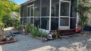 A covered outdoor area with a glass enclosure, surrounded by gravel and potted plants. - Cozy 2 Bedroom 1 Bath Canal Front Home On Ramrod Key (Ramrod Key)