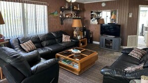 A living room with a black leather sofa, a coffee table, a television, and a ceiling fan. - Cozy 2 Bedroom 1 Bath Canal Front Home On Ramrod Key (Ramrod Key)