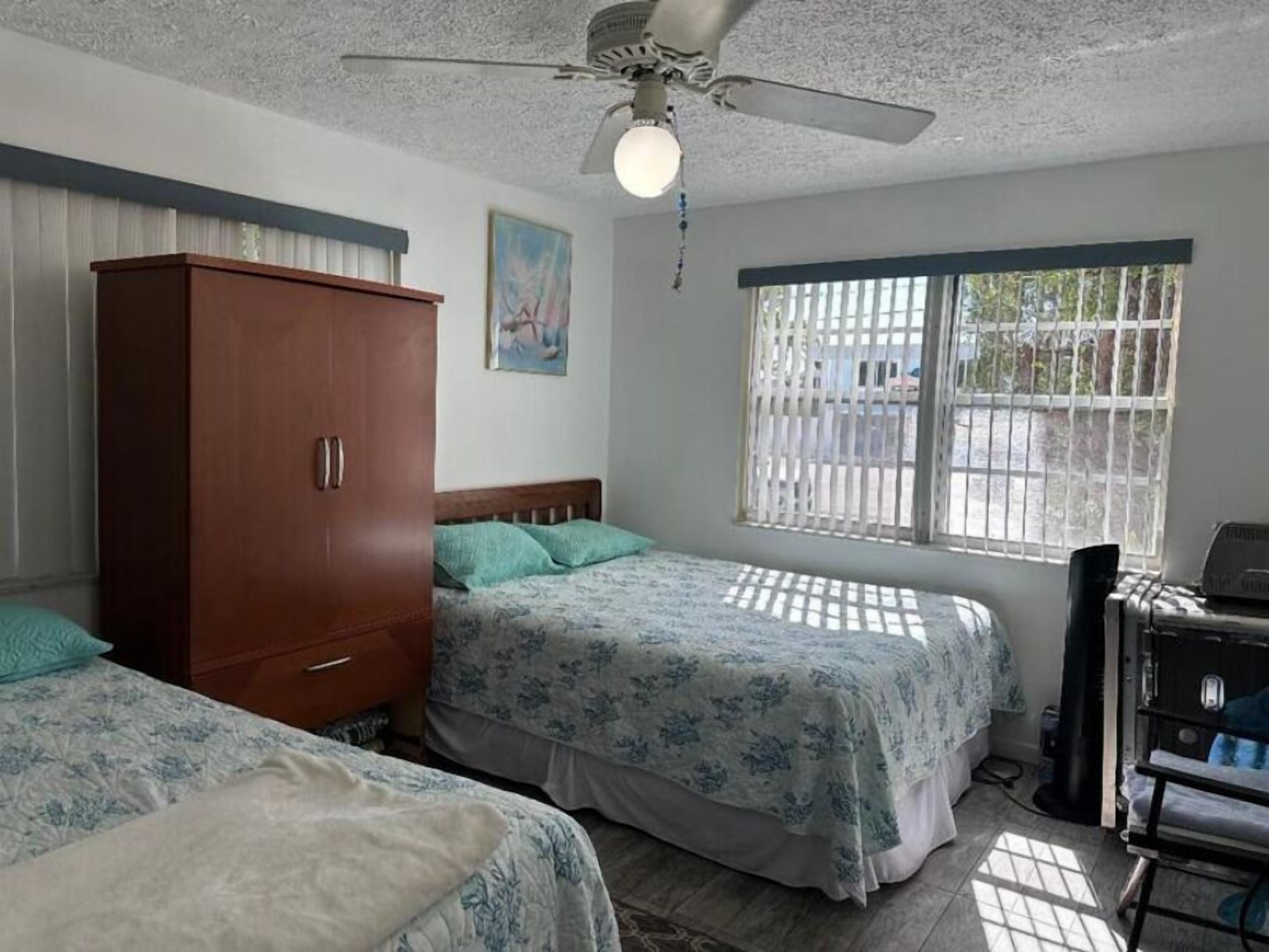 Un dormitorio con dos camas, un armario, un ventilador de techo y una ventana con barrotes.