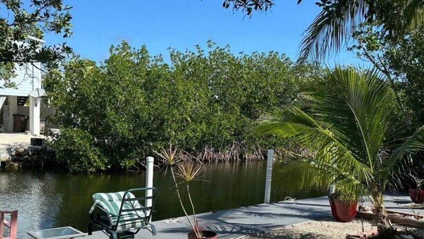 A waterfront patio with a table and chairs, surrounded by lush greenery and a calm body of water. - Cozy 2 Bedroom 1 Bath Canal Front Home On Ramrod Key (Ramrod Key)