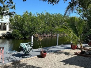 Une terrasse au bord de l’eau, avec une table et des chaises, entourée d’une végétation luxuriante et donnant sur une étendue d’eau calme.