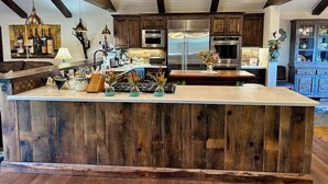 A kitchen with a large island, wooden cabinets, stainless steel appliances, and pendant lighting.