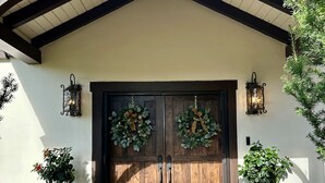 A wooden double door with two wreaths, flanked by two large blue planters, under a gabled roof.