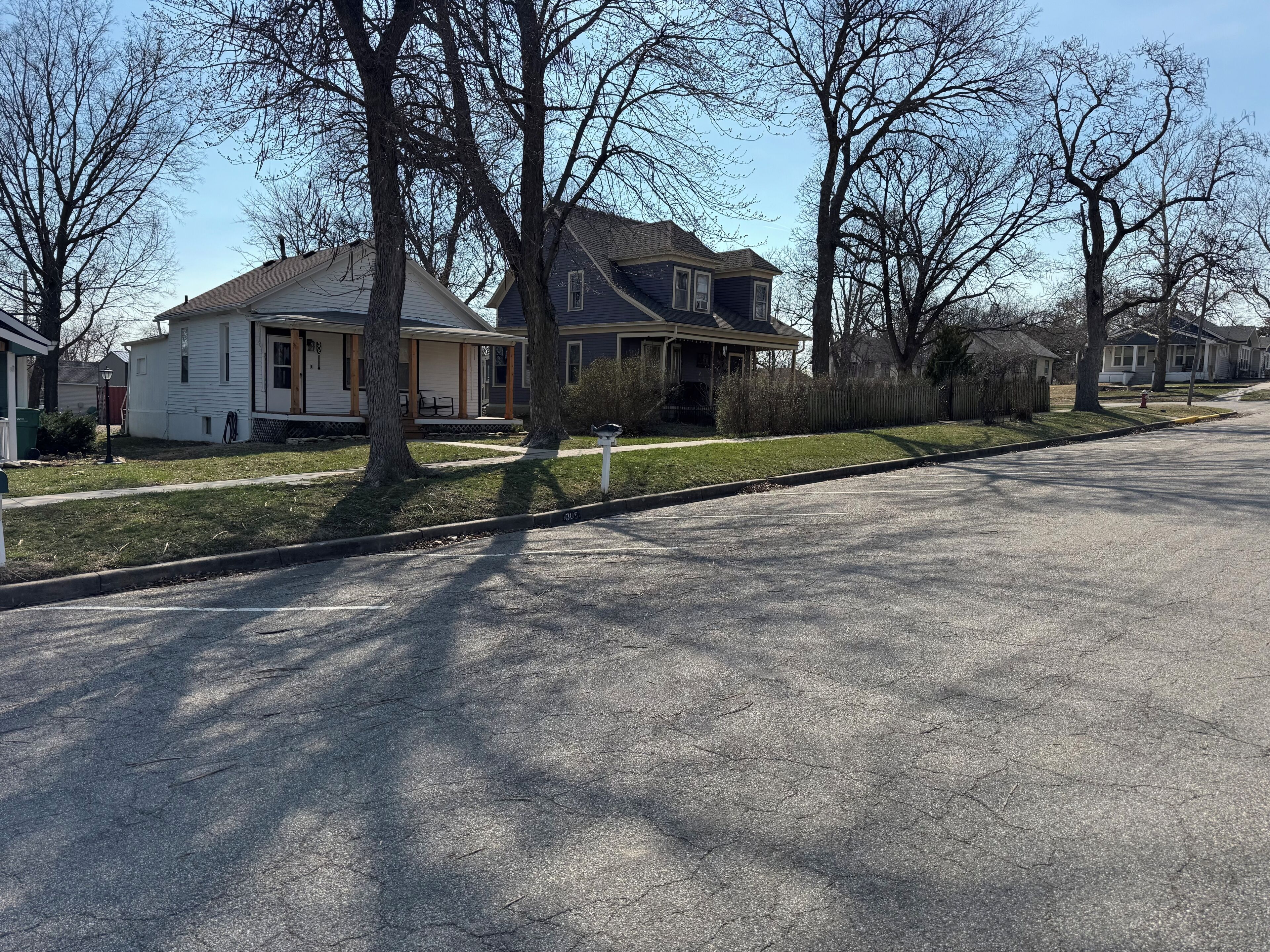 Une rue résidentielle bordée de maisons et d’arbres, avec un ciel dégagé.