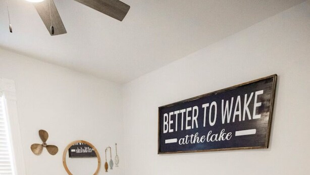 Een slaapkamer met een groot bed, een wandklok, een lijst met een citaat en een klein tafeltje met een lamp en beker.