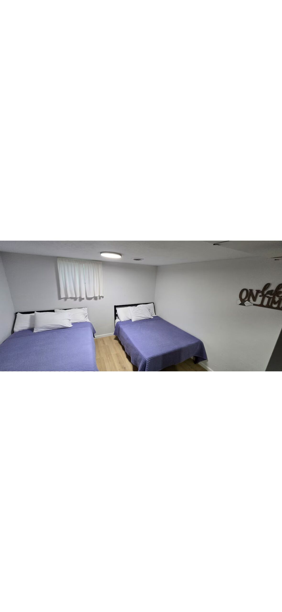 A room with two beds, white walls, and a ceiling light.