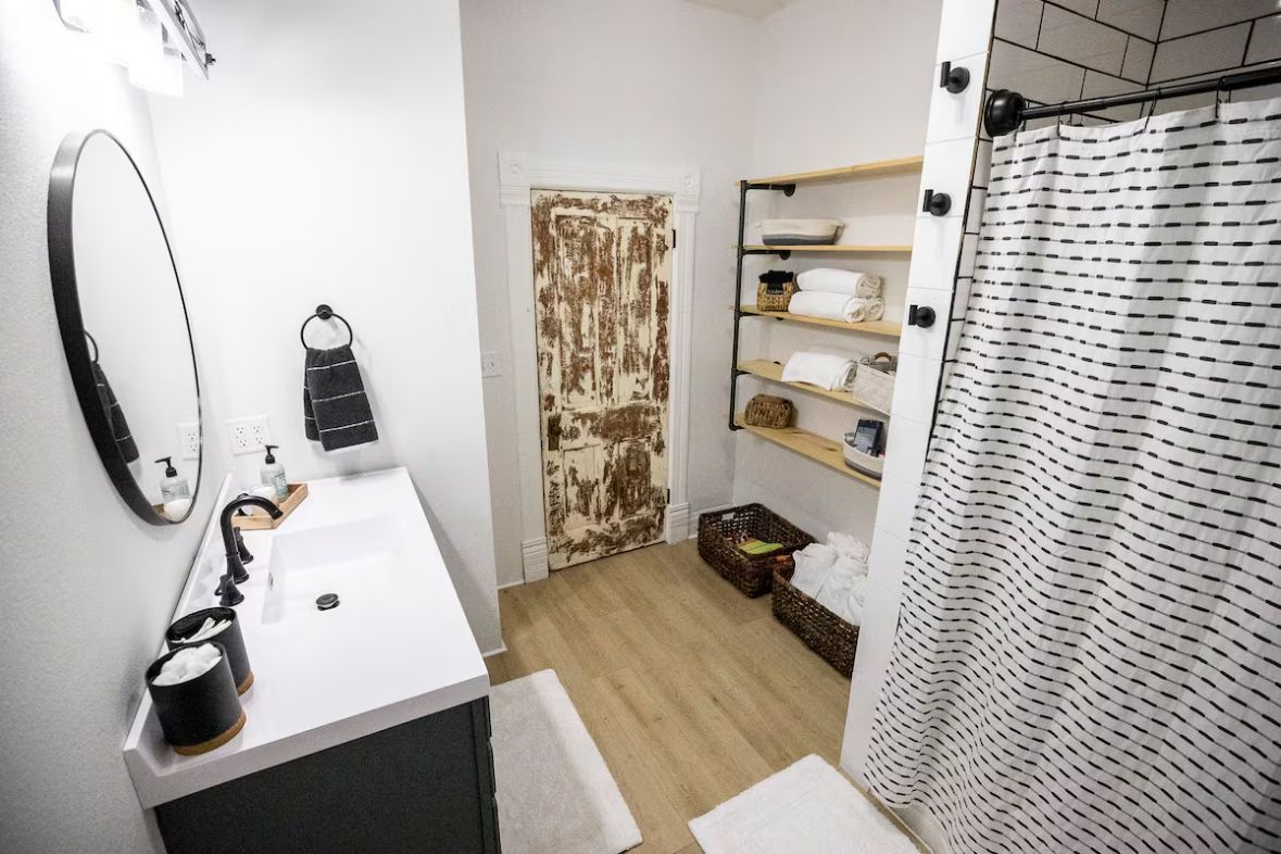 A bathroom with a white sink, a mirror, a towel rack, a shower curtain, and a shelf with toiletries.