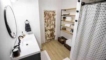 A bathroom with a white sink, a mirror, a towel rack, a shower curtain, and a shelf with toiletries.