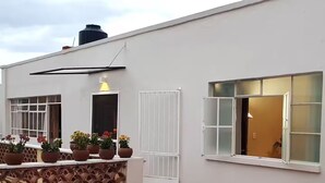 Un edificio blanco con múltiples ventanas, algunas con contraventanas, y un balcón con macetas.