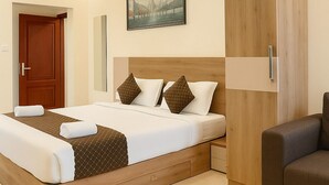 A modern hotel room with a large bed, a wooden wardrobe, a ceiling fan, and a painting on the wall. - Coastal Echoes Inn (Kochi)