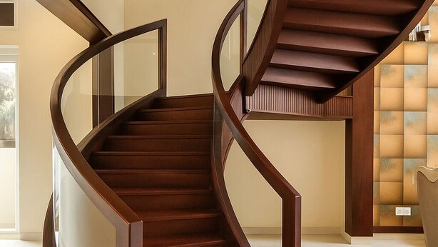 A modern spiral staircase with glass railings and wooden steps, leading to a second floor with a cushioned seating area. - Coastal Echoes Inn (Kochi)