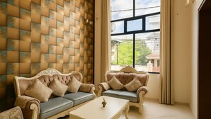 A room with two ornate sofas, a small table, and a large window with a view of buildings and greenery. - Coastal Echoes Inn (Kochi)