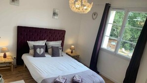 A bedroom with a large bed, two bedside tables, a chandelier, and a window with curtains. - Chambres d'hôtes Sous les Grands Chênes (Corcoue-sur-Logne)