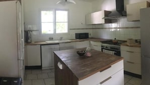 A compact kitchen with white cabinets, a wooden countertop, a microwave, a stove, and a window providing natural light. - Chambres d'hôtes Sous les Grands Chênes (Corcoue-sur-Logne)