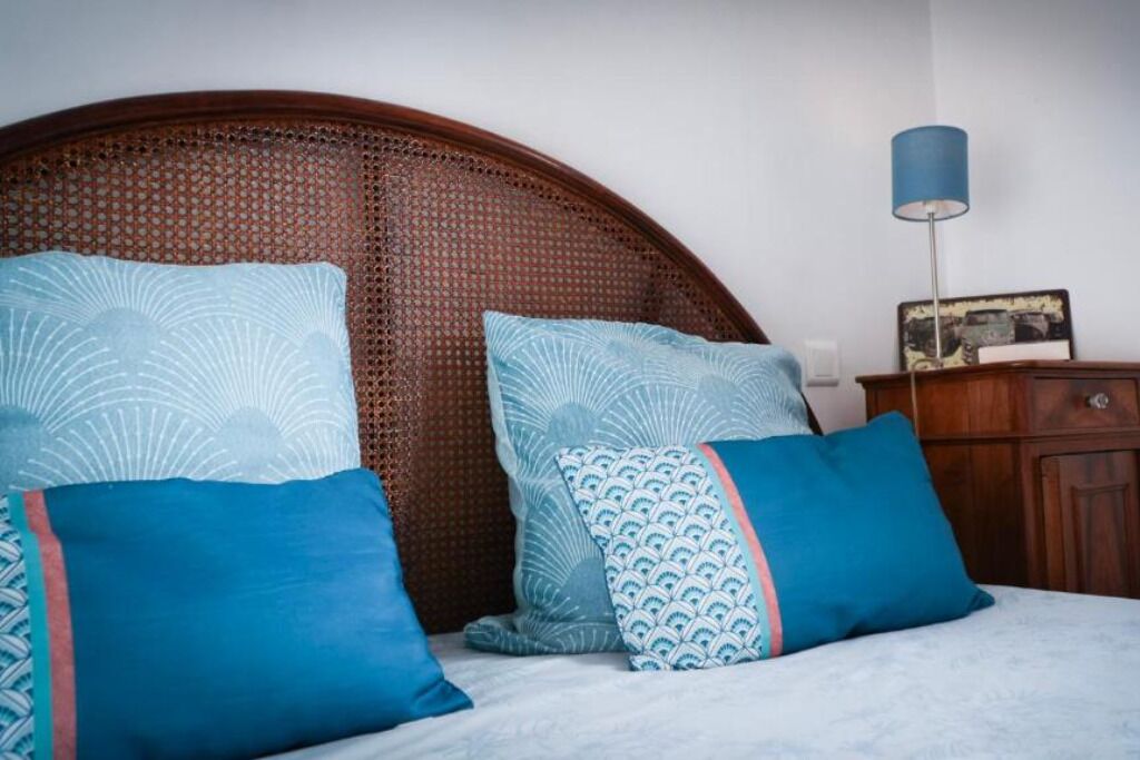 A bed with a woven headboard, two pillows, a bedside table, and a lamp.