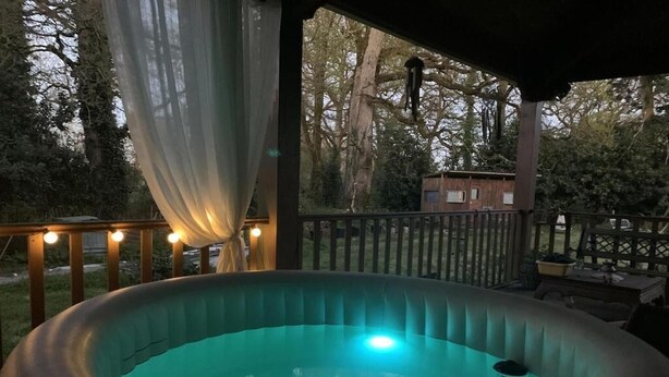 A hot tub under a covered area with a wooden deck and string lights. - Chambres d'hôtes Sous les Grands Chênes (Corcoue-sur-Logne)