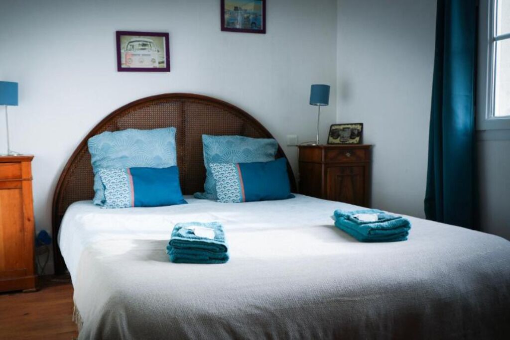 Un lit bien fait, agrémenté d’oreillers à motifs bleus et blancs, d’une tête de lit en bois et d’une petite table de chevet avec une lampe.