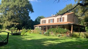 A two-story house with a porch, surrounded by a well-maintained lawn and trees. - Chambres d'hôtes Sous les Grands Chênes (Corcoue-sur-Logne)