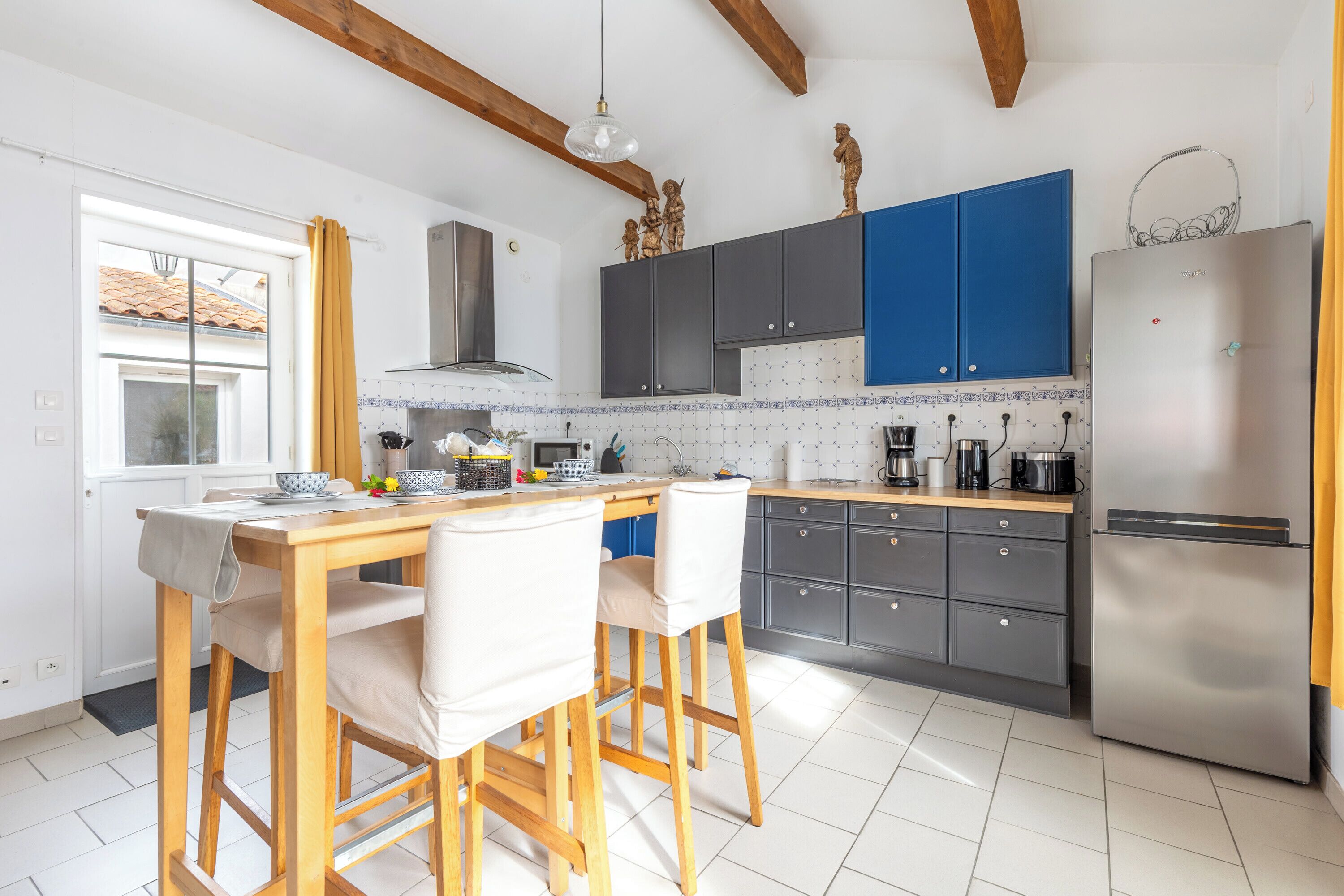 Een keuken met een houten tafel, twee stoelen, een koelkast en blauwe kastjes.