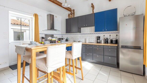 Una cocina con una mesa de madera, dos sillas, un refrigerador y armarios azules.