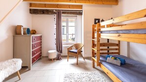 Una habitación acogedora con una litera, un aparador, una silla y un taburete pequeño.