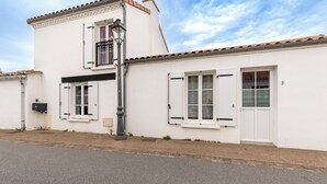 Un edificio blanco de dos pisos con techo de tejas, un balcón y una puerta con ventanal.