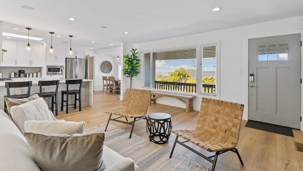 A modern living room with a sofa, two woven chairs, a small round table, and a large window with blinds. - @ Marbella Lane - 3BR W/sweeping Views of Bay Area (San Mateo)