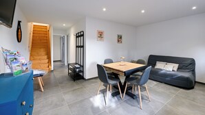 Ein modernes Wohnzimmer mit einer Holztreppe, einem Esstisch mit Stühlen, einem schwarzen Ledersofa und einem an der Wand befestigten Fernseher.