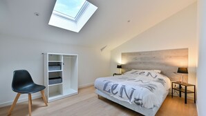 Ein Schlafzimmer mit Oberlicht, einem Bett mit Kopfteil, einem Nachttisch, einem Sessel und integrierten Regalen.