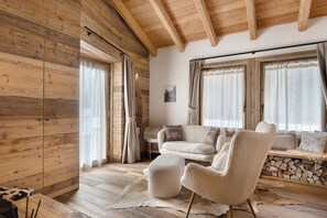 A cozy room with wooden walls, a sofa, chairs, and a fireplace.