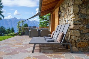 Un patio in pietra con una poltrona da relax e cuscini, un muro in pietra e vista sulle montagne.
