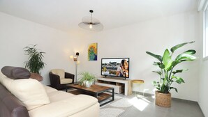 A modern living room with a sofa, a coffee table, a TV, and potted plants. - Le Debussy - Wifi - Parking - Centre (Laval)