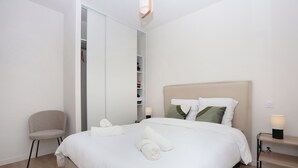 A neatly arranged hotel room with a bed, a chair, a bedside table with a lamp, and a wardrobe. - Le Debussy - Wifi - Parking - Centre (Laval)