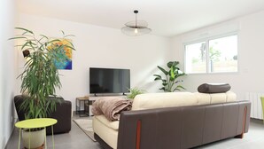 A modern living room with a sofa, a TV, a plant, and a window. - Le Debussy - Wifi - Parking - Centre (Laval)