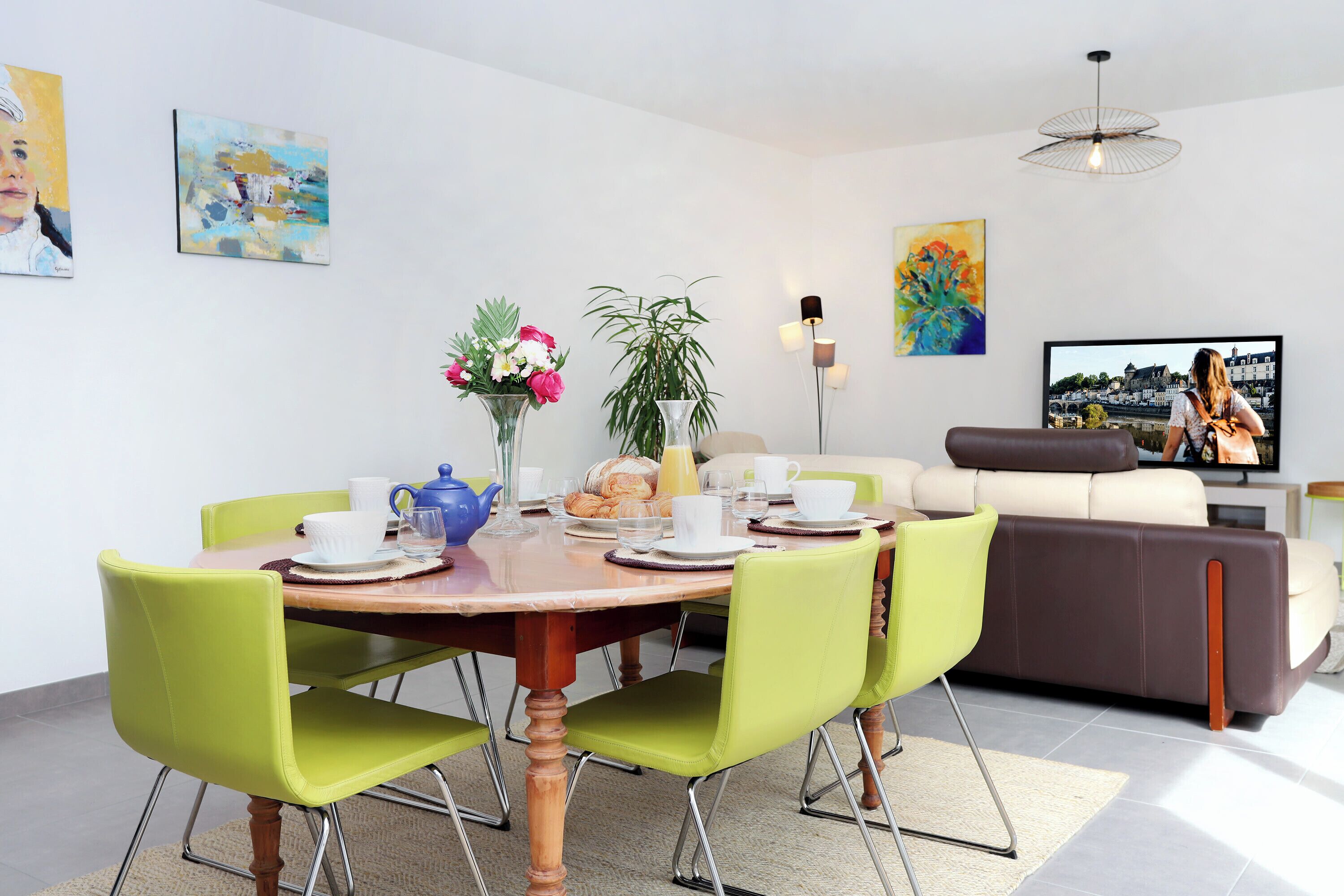 Una sala de estar moderna con comedor, que incluye una mesa redonda de madera, sillas verdes, un sofá y un televisor de pantalla plana.