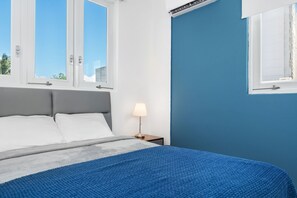A bedroom with a bed, two windows, a nightstand, and a lamp. - Near the Water Shared Pool Pets Permitted (San Juan)