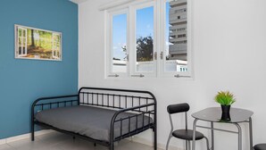 A room with a bed, a small table with a plant, and a window with a view of buildings. - Near the Water Shared Pool Pets Permitted (San Juan)