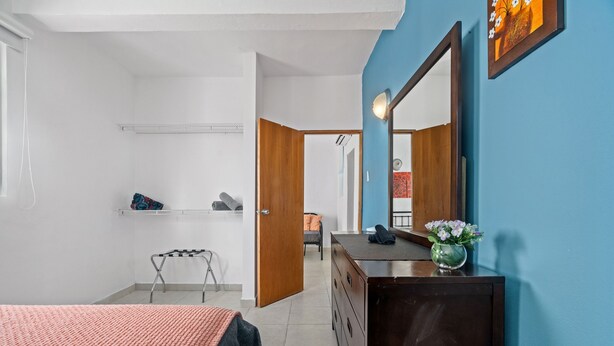 A bedroom with a bed, a dresser, a mirror, and a small table with a vase of flowers.